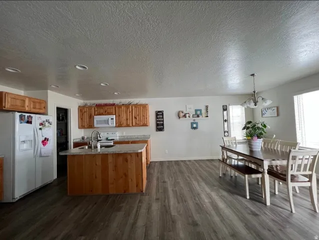 Kitchen and dining area featuring wood-finish flooring, recessed lighting, wood cabinetry, a kitchen island with sink, and a multi-light chandelier