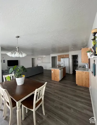 Wood-finish flooring throughout, kitchen island with built-in sink, stainless steel refrigerator, and wood cabinetry