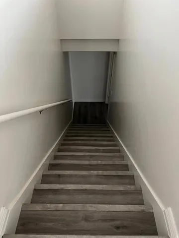 Staircase featuring wood-finish treads and risers, white walls, and a white handrail