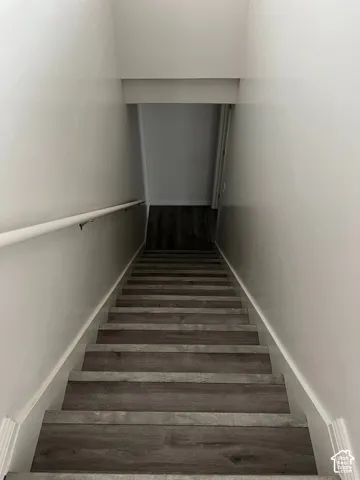 Staircase featuring wood-finish treads and risers, white walls, and a white handrail