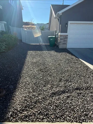 Gravel driveway with a white garage door, stone veneer accents, and a privacy fence