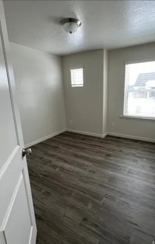 Wood-finish flooring, white walls, two windows with blinds, and a flush mount ceiling light fixture