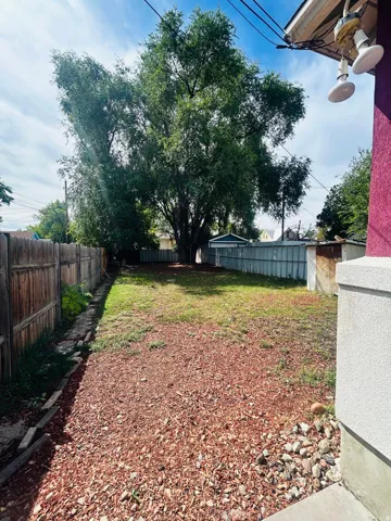 Spacious backyard featuring a large tree, partial wood fencing, and a partial metal fence
