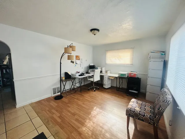 Wood-finish flooring with a tile entry, white painted walls, and a window with blinds