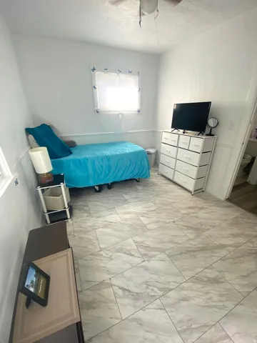 Light-colored tile flooring, window with natural light, ceiling fan, and wainscoting