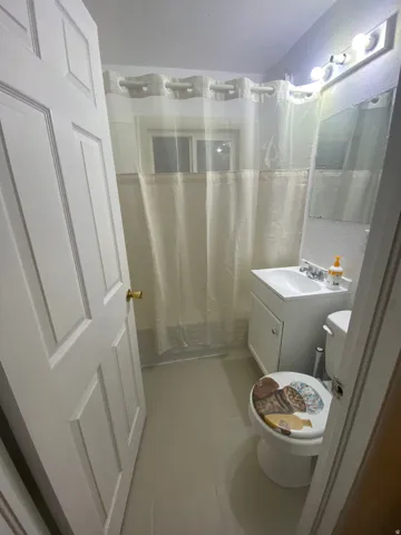 Panel interior door, vanity with integrated sink, wall-mounted mirror, overhead lighting fixture, and tile flooring
