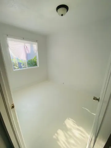 White painted walls, white painted flooring, and a single window with blinds
