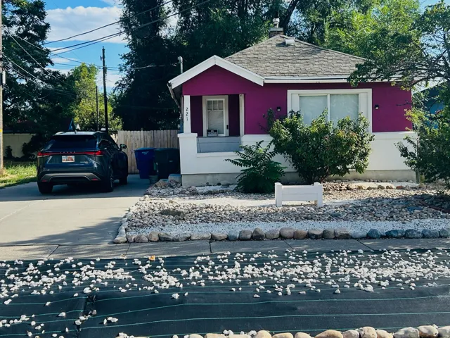 Single-story residence featuring a vibrant magenta and white exterior, a covered front porch, and a gray shingle roof