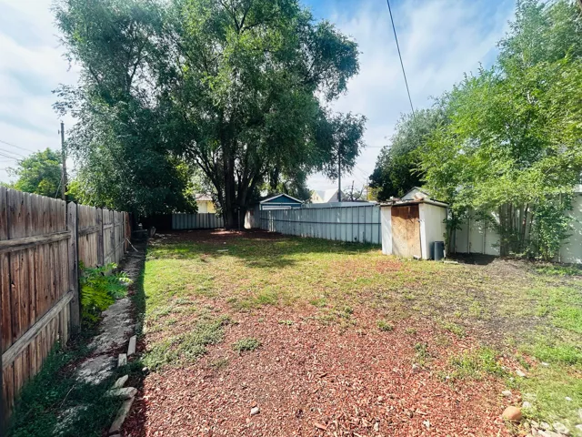 Expansive backyard featuring a large tree, partial wood fencing, and a storage shed