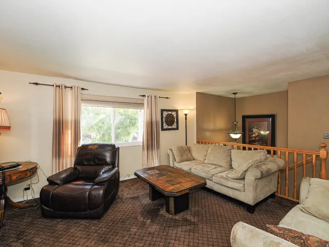 Carpeted living area featuring a large window, spindle railing, and a pendant light fixture