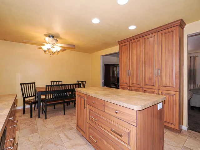 Expansive wood-finish cabinetry, central island with countertop, recessed lighting, and tile flooring