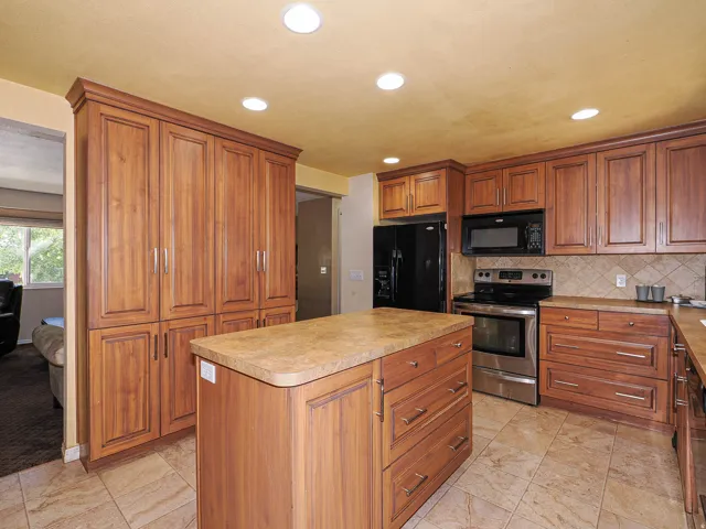 Kitchen featuring wood cabinetry, a central island with countertop, tile flooring, and integrated black appliances