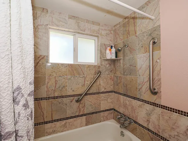 Bathtub with tiled surround, mosaic tile accent, and built-in shower shelf