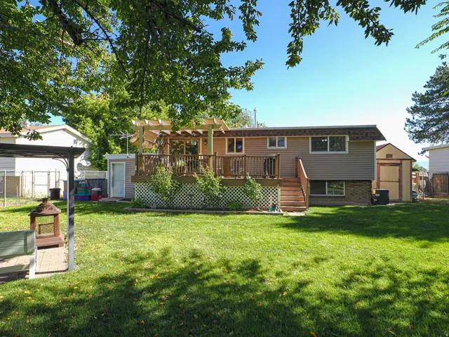 Expansive backyard featuring a manicured lawn, a wooden deck with railing, and a slatted pergola
