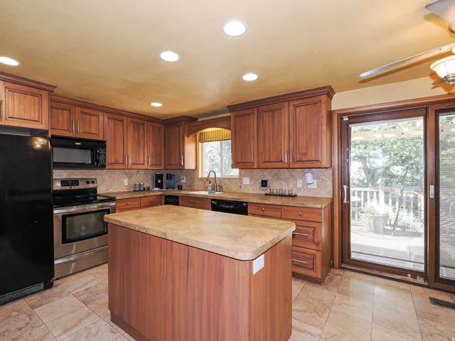 Kitchen featuring wood-finish cabinetry, a central island, tile flooring, stainless steel appliances, and a glass sliding door leading to an outdoor deck
