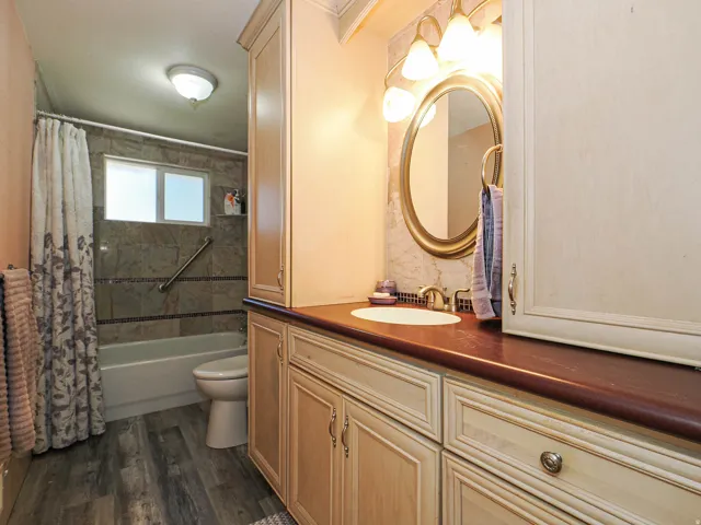 Bathroom featuring wood-finish flooring, a built-in vanity with a single basin sink, a large mirror with overhead lighting, and a tiled shower-tub combination