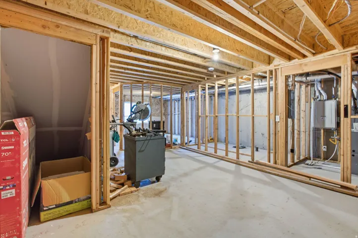 Unfinished basement featuring wood framing, exposed joists, concrete flooring, and visible utility connections