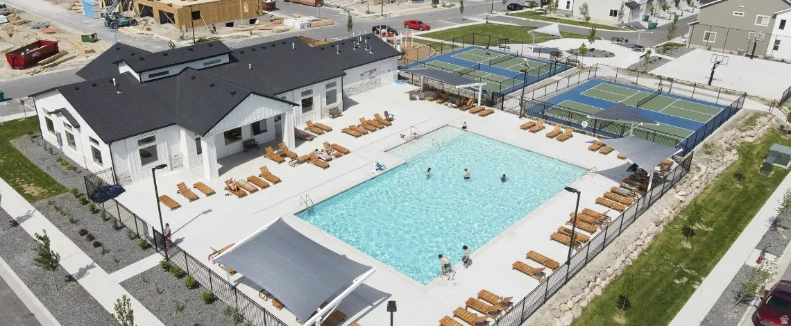 Community clubhouse with a large swimming pool, expansive pool deck, and adjacent sports courts