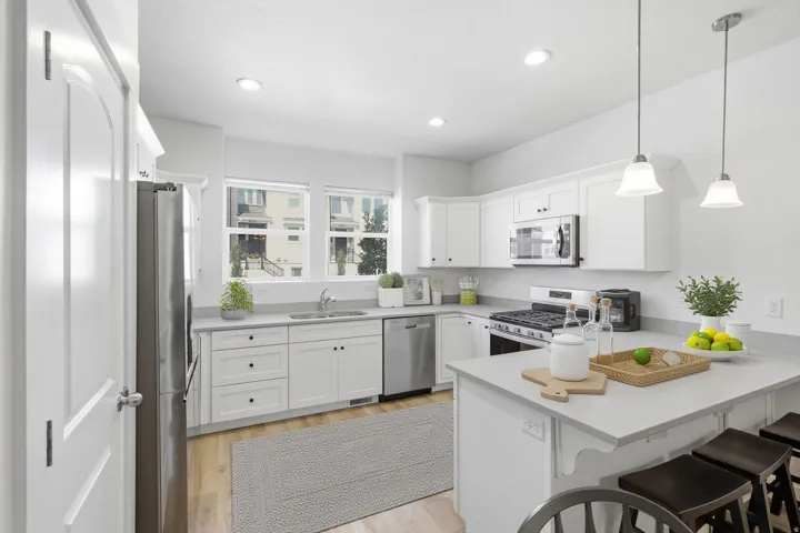 Modern kitchen featuring light wood-finish flooring, white cabinetry, integrated stainless steel appliances, and a central island with pendant lighting