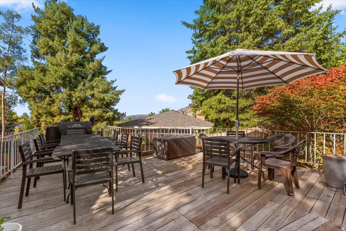 Expansive wood-finish deck with white metal railings, surrounded by mature trees and colorful foliage