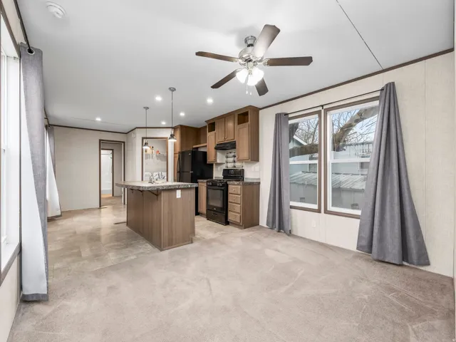 Open concept living area featuring a kitchen island with sink, wood-finish cabinetry, black appliances, and pendant lighting