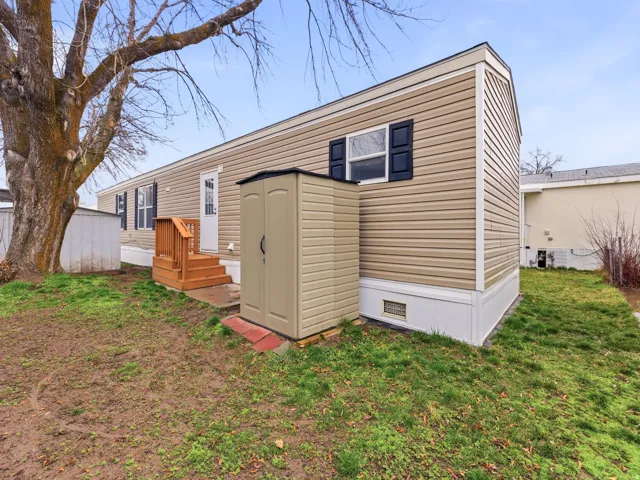 Tan horizontal siding with white trim, black window shutters, a wooden deck with steps, and an exterior storage shed