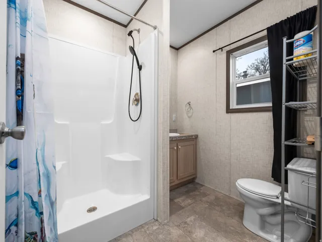 Shower stall with integrated seating, single vanity with wood-finish cabinetry, and window with dark trim