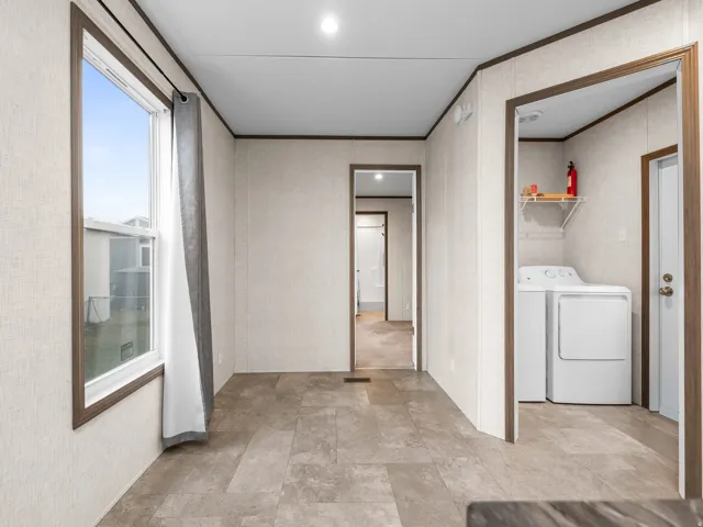 Spacious utility corridor featuring tile flooring, abundant natural light from large window with thermal-pane framing, and direct access to laundry appliances including washer and dryer