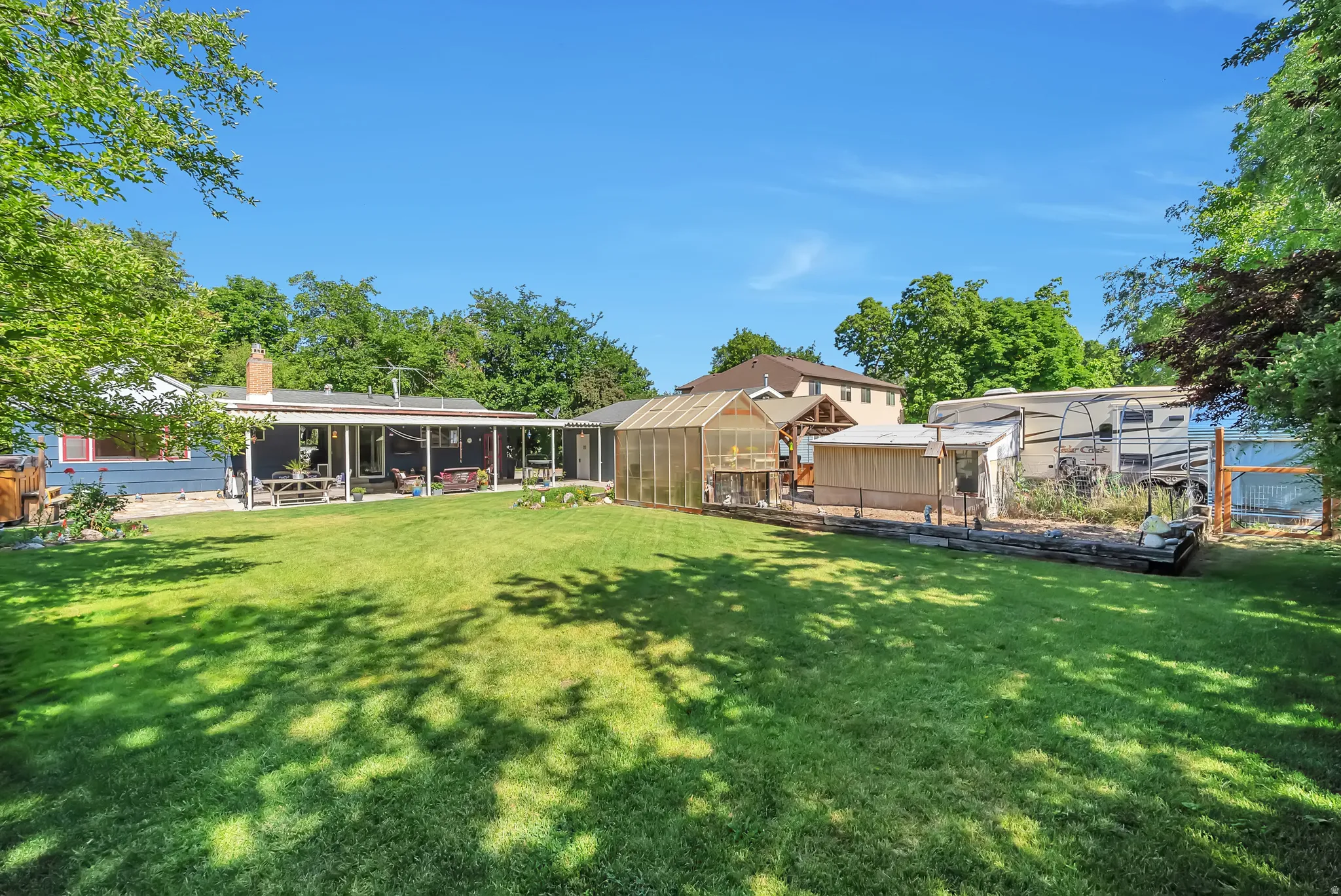 Expansive backyard with a manicured lawn, a covered patio, a greenhouse structure, and raised garden beds