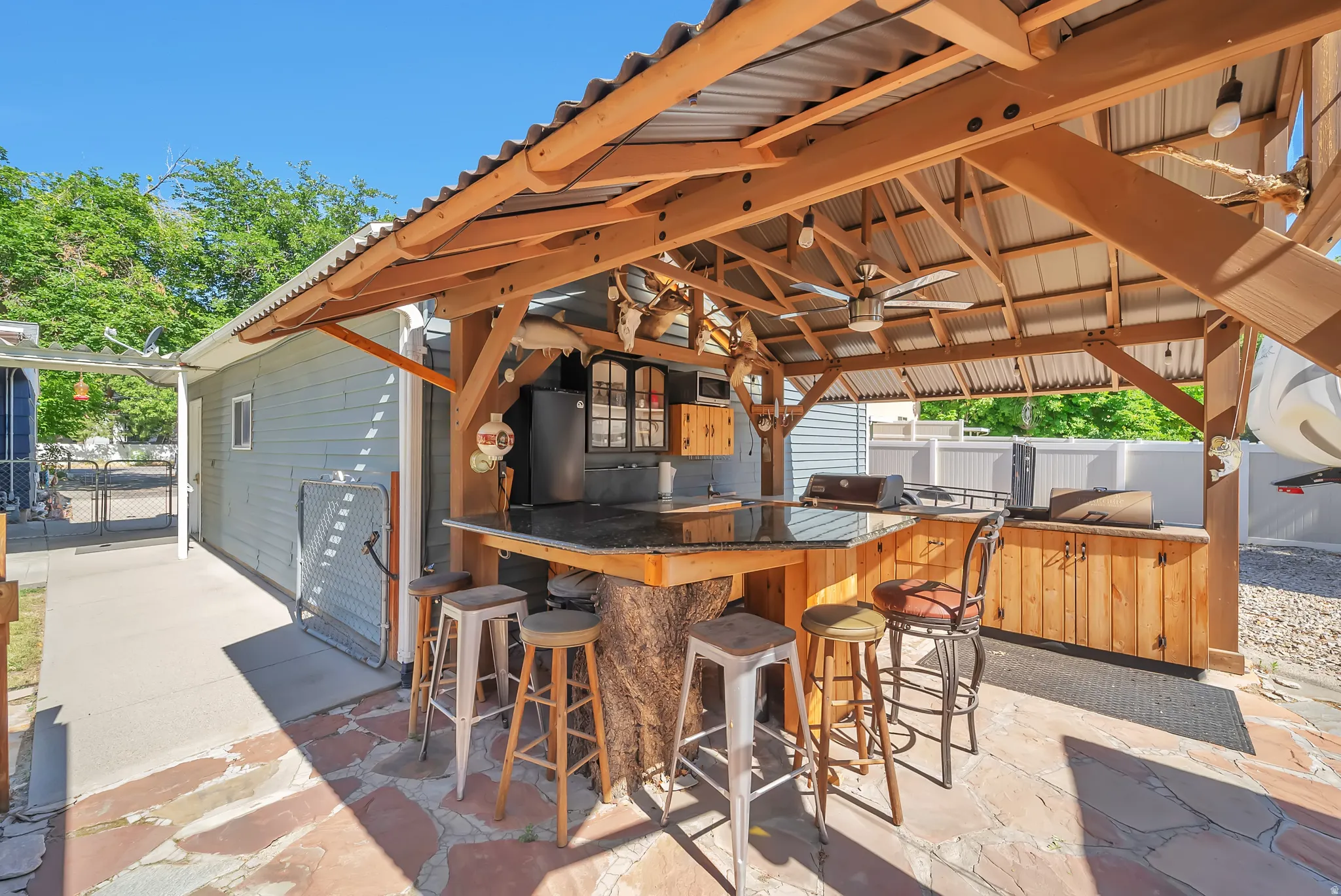 Outdoor kitchen with a corrugated metal roof, wood-beam construction, and a ceiling fan