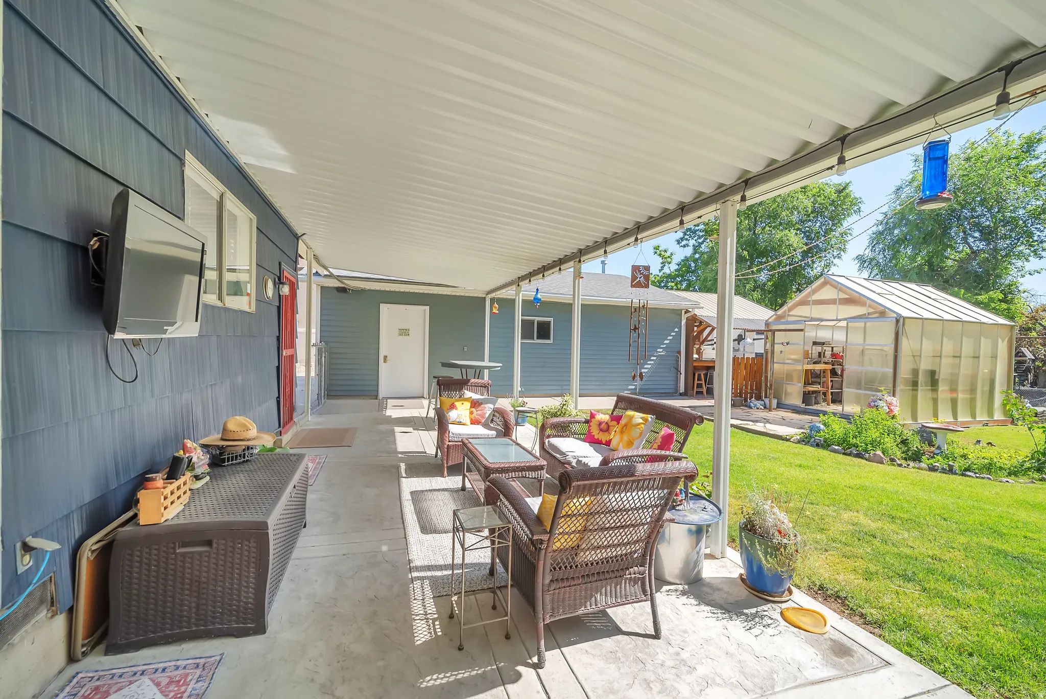 Expansive covered patio with concrete flooring, siding exterior, and a detached greenhouse structure