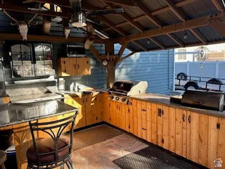 Covered outdoor kitchen featuring a built-in grill, corrugated metal roof, wood cabinetry, and an outdoor ceiling fan