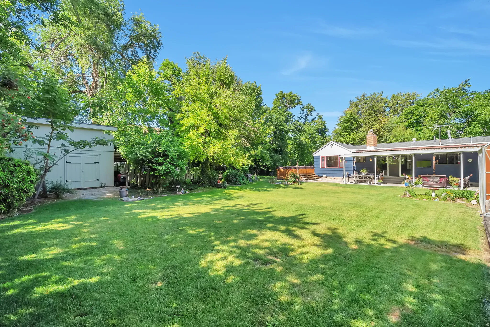 Expansive green lawn, mature trees, detached storage shed, covered patio, and raised wood deck