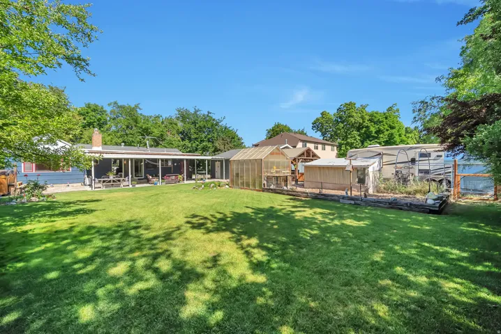 Expansive backyard with a manicured lawn, a covered patio, a greenhouse structure, and raised garden beds