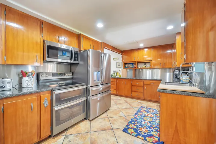 Wood cabinetry with ample storage, stainless steel appliances, dark stone countertops, tile flooring, and recessed ceiling lighting