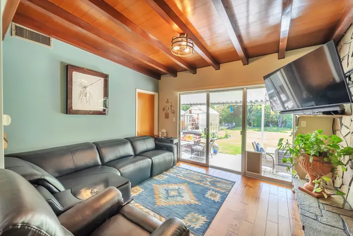 Exposed wood beam ceiling, wood-finish flooring, full-light sliding glass door, and stone-faced fireplace with hearth