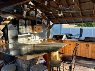 Outdoor kitchen featuring a built-in grill, wood cabinetry, dark countertops, and a ceiling fan
