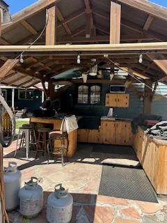 Outdoor covered patio featuring an exposed beam ceiling, stone flooring, built-in wooden cabinetry, and a ceiling fan