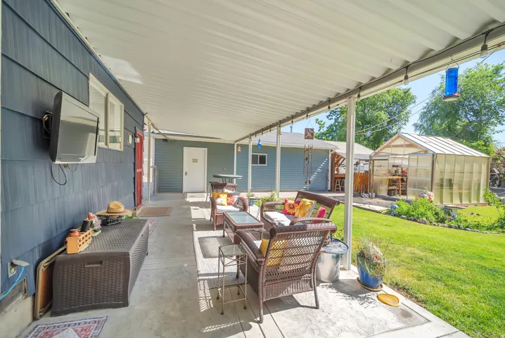Expansive covered patio with concrete flooring, siding exterior, and a detached greenhouse structure
