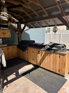 Outdoor kitchen featuring a wood-finish cabinet base, stone tile flooring, and a corrugated metal roof