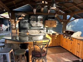 Outdoor kitchen with a built-in grill, stone-finish countertops, wood cabinetry, and an overhead ceiling fan