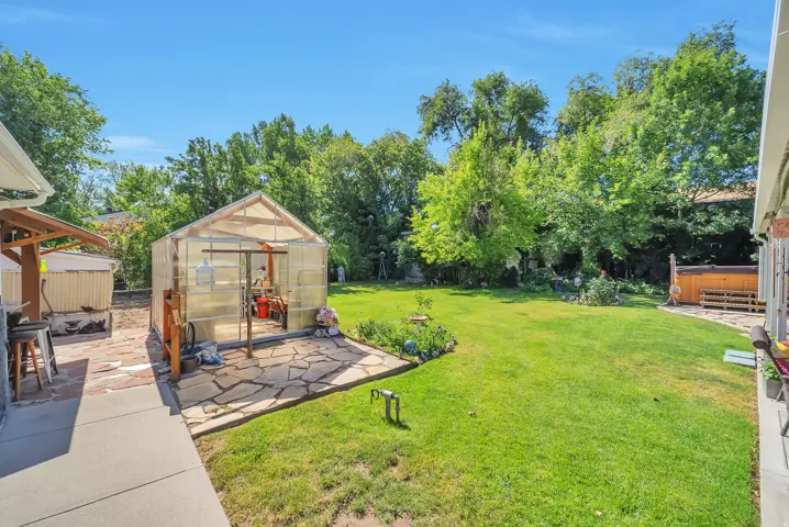 Expansive backyard featuring a lush lawn, mature trees, a greenhouse, and a flagstone patio