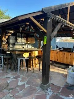 Outdoor bar structure featuring a corrugated roof, exposed wood beams, a built-in bar, wood cabinetry, and flagstone paving