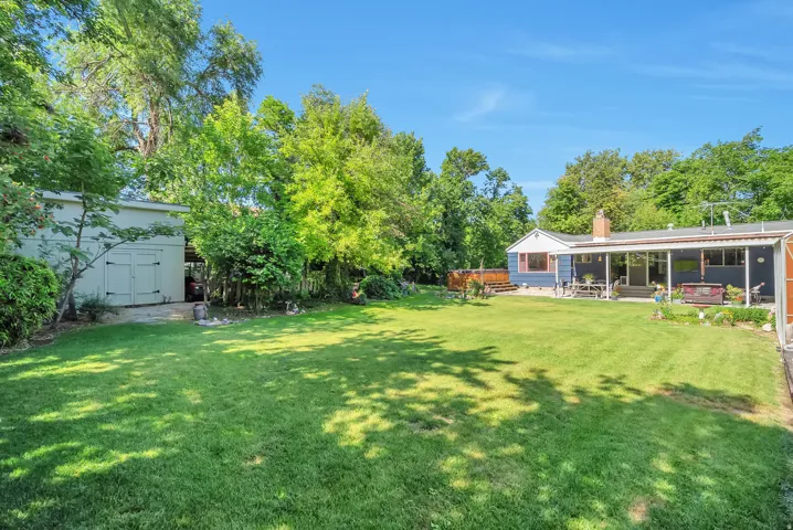 Expansive green lawn, mature trees, detached storage shed, covered patio, and raised wood deck
