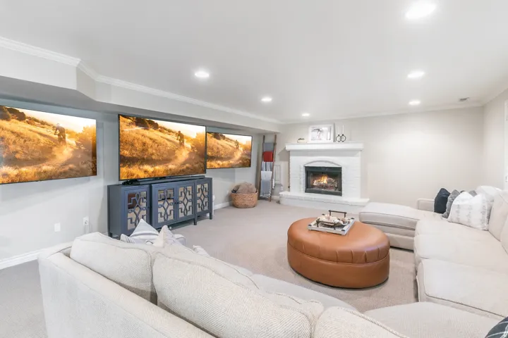 Recessed lighting, crown molding, a brick fireplace, and wall-mounted media storage with patterned doors