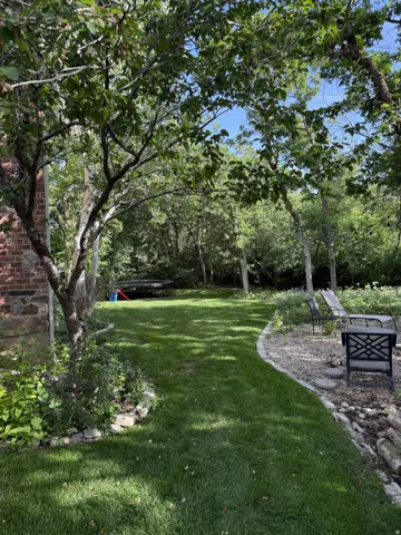 Expansive lawn area, mature trees, brick exterior, stone garden edging, and a gravel patio