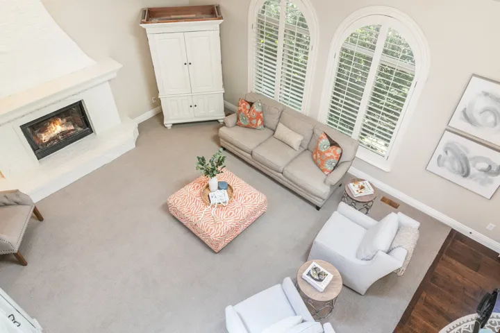 Carpeted living area featuring an architectural fireplace, arched windows with plantation shutters, and light-toned wall paint