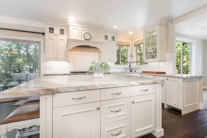 Kitchen featuring an expansive island with a light-toned countertop, white cabinetry with decorative hardware, dark wood-finish flooring, and recessed lighting