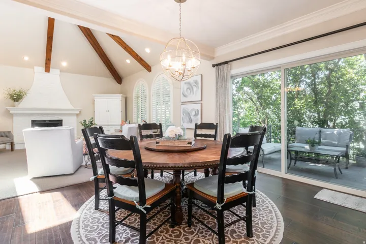 Vaulted ceiling with exposed wood beams, white brick fireplace, wood-finish flooring, sliding glass doors, and recessed lighting
