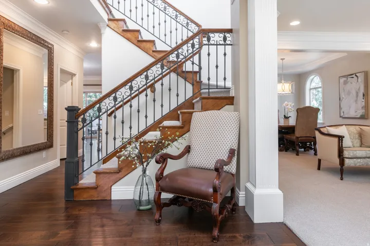 Hardwood flooring, custom wrought iron stair railing, recessed lighting, arched window, and decorative column
